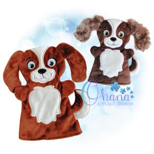 May include: Two plush dog hand puppets. The puppets are brown and white with floppy ears, embroidered facial features, and white chest patches. The puppets have a friendly, cartoonish appearance. The image includes the text "Ohana Applique Designs".