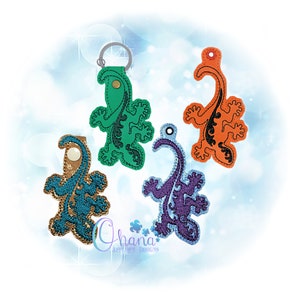 May include: Four different colored keychains featuring a lizard design. The keychains are green, orange, blue, and purple.