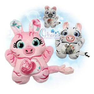 May include: Three plush animal toys in the image. One is pink with a rose design, and two are white with black stripes. The toys have large eyes and are designed with an embroidered style. The text "Chana Applique Designs" is also visible.