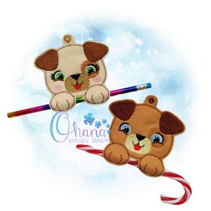 May include: Two embroidered felt dog ornaments. One is holding a pencil and the other is holding a candy cane. Both dogs have brown and white fur with brown noses and blue eyes.