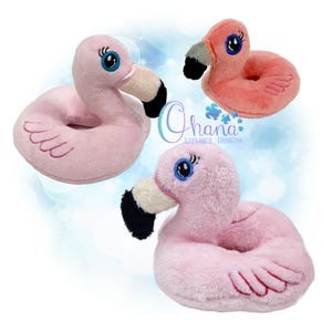 May include: Three plush flamingo toys in varying shades of pink. Each flamingo has a black and white beak, blue eyes, and a ring-shaped body. The text "Ohana Applique Designs" is visible in the image.