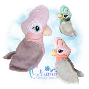 May include: Three plush bird toys in pink, green, and gray. The birds have detailed embroidered eyes, beaks, and crests. The plush toys are in various sizes and orientations, with the largest one on the left.