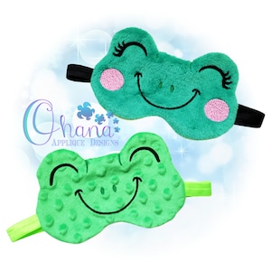 May include: Two green frog-shaped sleep masks with embroidered smiling faces. One mask has a textured surface and the other has a smooth surface.