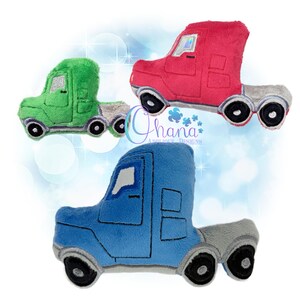 May include: Three plush toy semi-trucks in red, green, and blue. Each truck has a grey trailer, black wheels, and a silver-coloured windscreen. The trucks are soft and fluffy, with embroidered details. The image includes the text "Ohana Applique Designs".