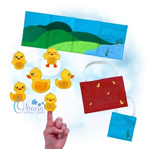 Könnte beinhalten: Ein Fingerpuppen-Set aus Filz mit fünf gelben Enten, jede mit einer Nummer auf der Brust. Die Enten sind in einer Reihe angeordnet, mit der Nummer eins Ente links und der Nummer fünf Ente rechts. Das Set enthält auch eine Filztafel mit einem grünen Hügel und einem blauen Teich sowie eine rote Filztasche mit der Aufschrift "5 kleine Enten" bestickt.