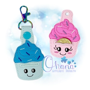 May include: Two cupcake-shaped keychains. One is blue with blue sprinkles and a silver clasp. The other is pink with pink sprinkles and a coin inside. Both have smiling faces and are made of felt.