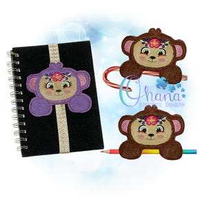 May include: Two embroidered monkey bookmark designs. One is purple with a flower crown and the other is brown with a flower crown. Both are holding a pencil.