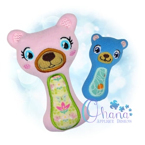 以下が含まれることがあります： クマの形をしたぬいぐるみのおしゃぶり2個。1つはピンクで花柄、もう1つはブルーでバスケットボール柄。どちらも刺繍された目と鼻があります。