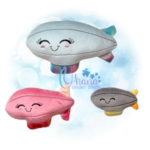 May include: Three plush toy blimps with smiling faces. The blimps are in different colors: light blue, pink, and gray. The blimps have a rainbow pattern on the bottom.