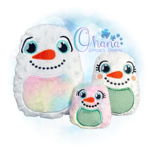 May include: Three snowman plush toys in varying sizes. The snowmen have white bodies with colorful bellies, orange carrot noses, and black smiles. The eyes are large and blue. The text "Ohana Applique Designs" is in the background.