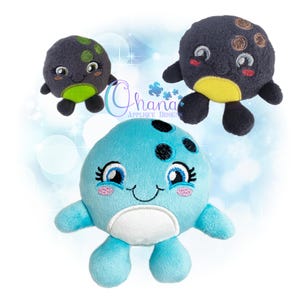 May include: Three plush, round, cartoon-style sea creatures with embroidered details. One is light blue with a white belly, one is dark gray with a green belly, and one is dark gray with a yellow belly. Each has large eyes and fins.