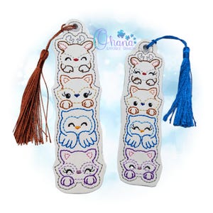 May include: Two white bookmarks with embroidered animal designs. Each bookmark features a stack of four animals: a bear, fox, owl, and cat. One has a brown tassel, the other a blue tassel. The text "Ohana Applique Designs" is visible.