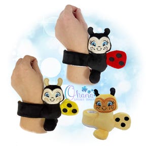 May include: Three plush insect wristbands: a ladybug with red wings and black spots, a bee with yellow accents, and a yellow insect with black spots. Each wristband has a black cuff.