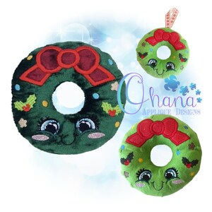 May include: Three plush Christmas wreath ornaments. The wreaths are green with a red bow, holly accents, and a smiling face with blue eyes. One wreath has a ribbon for hanging. The text "Ohana Applique Designs" is visible.