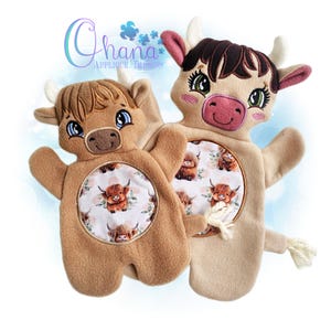 May include: Two plush Highland cow hand puppets. One is light brown, the other is tan. Both have embroidered faces, small horns, and a circular patterned belly with a Highland cow illustration. The puppets have a soft, fuzzy texture.