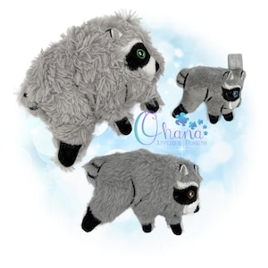 May include: Three plush raccoon appliques in varying sizes, featuring grey shaggy fabric, black eye masks, white facial accents, and black paws. The text Ohana APPLIQUE DESIGNS is visible in the centre, accompanied by a small blue floral graphic.