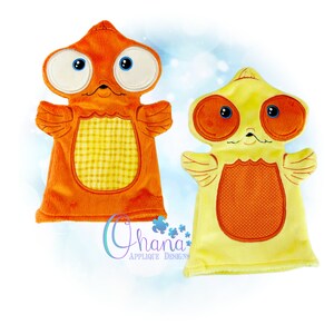 Puede incluir: Dos marionetas de mano de peluche con forma de peces de dibujos animados. Una es naranja con una barriga de cuadros amarillos, la otra es amarilla con una barriga de lunares naranjas. Ambas tienen ojos grandes, pequeñas alas y están etiquetadas como "Ohana Applique Designs".