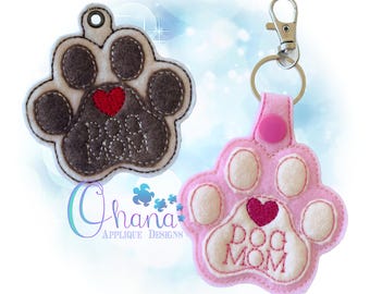 May include: Two felt paw print keychains. One is brown with a red heart and the text "Dog Mom". The other is pink with a pink heart and the text "Dog Mom".