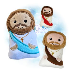 Può includere: Tre figure di peluche di Gesù Cristo, ognuna con barba e capelli castani, che indossano vesti bianche. Una figura ha una fascia blu, un'altra una fascia rossa e la terza una fascia marrone. Ogni figura ha una collana con una croce d'oro.