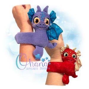 Könnte beinhalten: Zwei Plüsch-Drachen-Armbänder. Der lila Drache hat blaue Flügel und orange Augen. Der rote Drache hat gelbe Flügel und rote Augen. Beide Drachen haben ein lächelndes Gesicht.