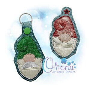 May include: Two gnome-shaped keychains made of textured material. One features a green glitter hat and a silver coin in a pocket, with a metal ring and green snap. The other has a red glitter hat and a small red star at the top. Text reads Ohana Applique Designs.