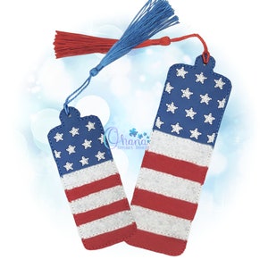 May include: Two patriotic bookmarks featuring the American flag design. Each bookmark has a blue top with white stars and red and white stripes. They are adorned with blue and red tassels.