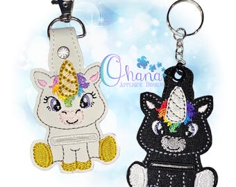 May include: Two unicorn keyrings. One is white with a gold horn and rainbow mane, the other is black with a white horn and rainbow mane. Both have a silver clasp or keyring. The keyrings are embroidered with a smiling face.