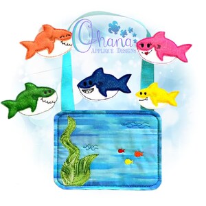 May include: A blue felt bag with a turquoise strap and five felt shark appliques. The sharks are orange, pink, green, blue, and yellow. The bag has a blue felt pocket with a green seaweed applique and a blue and white striped background. The text "Ohana Applique Designs" is on the bag.