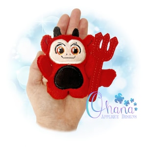 Puede incluir: Un muñeco de diablo de felpa rojo con vientre negro, cuernos negros y un tridente rojo. El muñeco tiene una cara blanca con ojos bordados y una boca sonriente. El muñeco se sostiene en una mano.