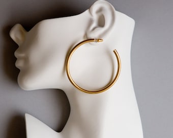 May include: A gold hoop earring on a white mannequin head.