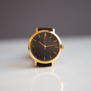 May include: A gold wristwatch with a black face and brown leather band.