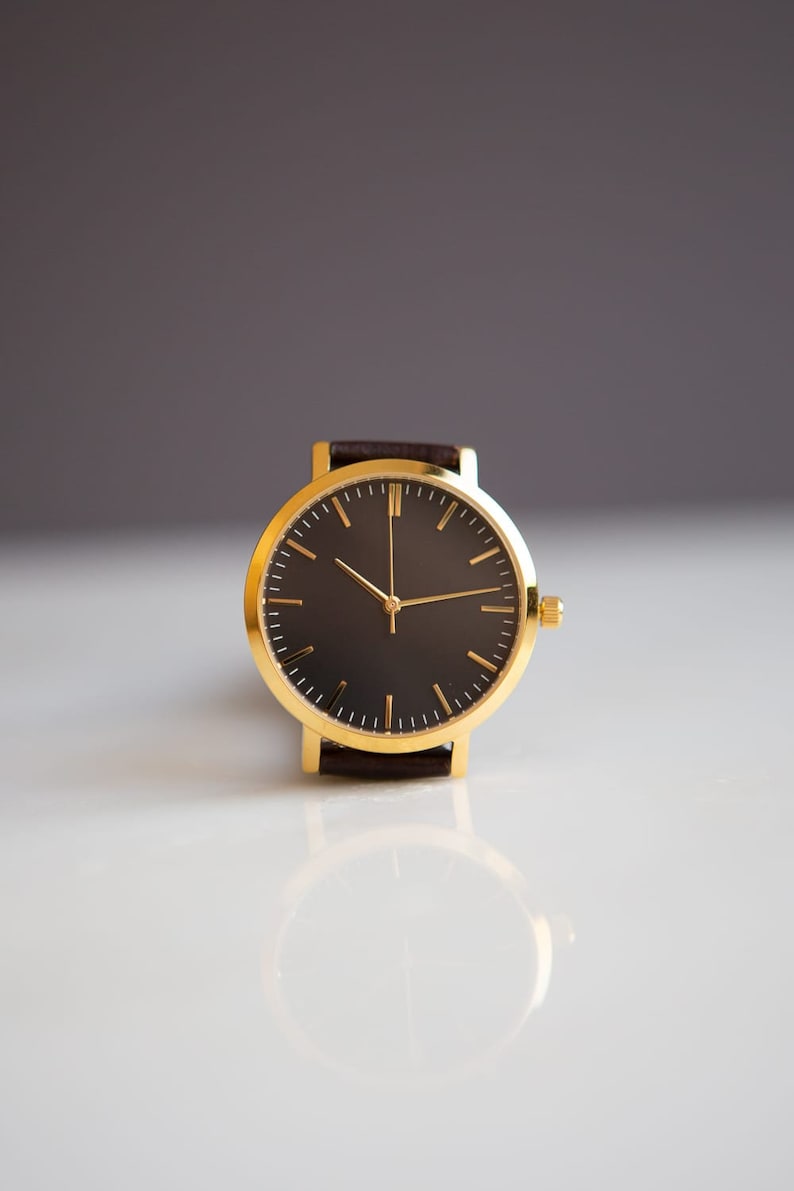 May include: A gold wristwatch with a black face and brown leather band.