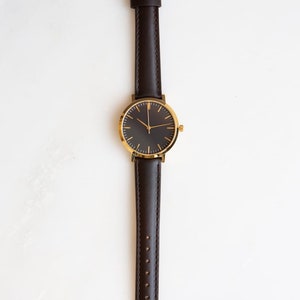 May include: A gold-tone watch with a black face and brown leather band.