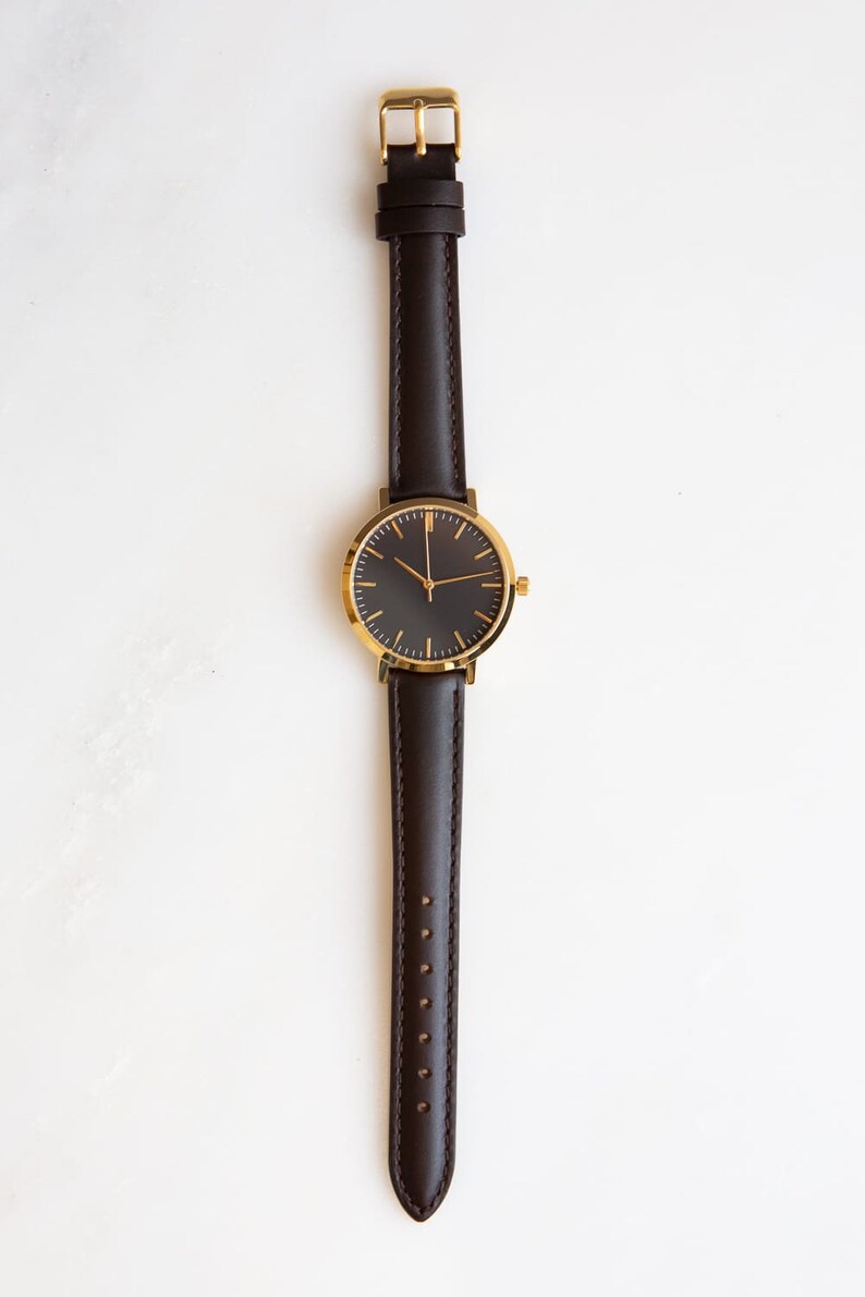 May include: A gold-tone watch with a black face and brown leather band.