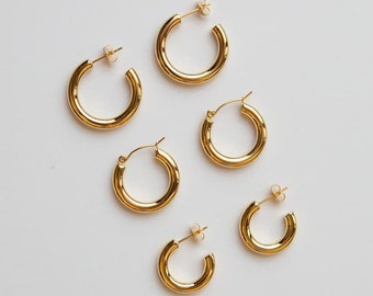 May include: Five gold hoop earrings of varying sizes. The earrings are all made of a thick, round wire.