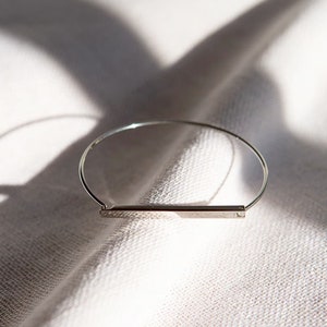 May include: A silver bangle bracelet with a thin, rectangular bar in the center.