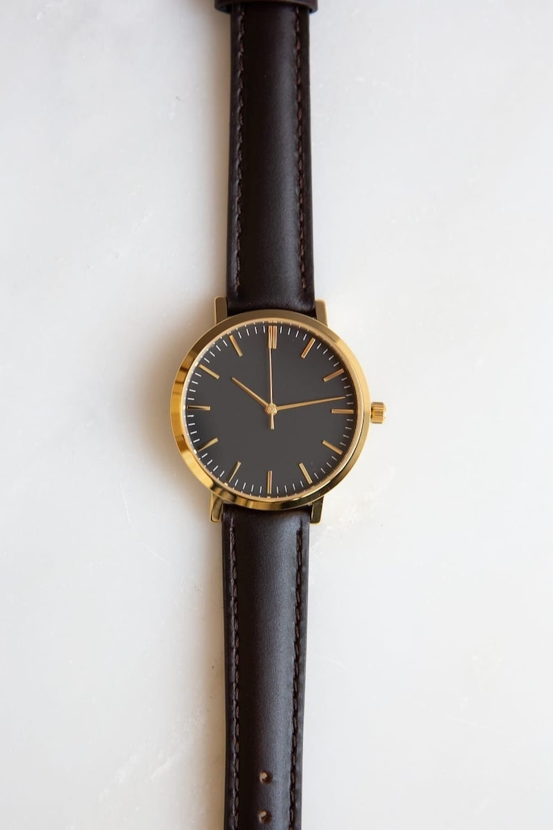 May include: A gold-tone watch with a black face and brown leather band.