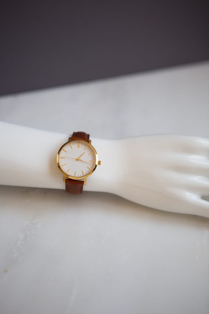 May include: A gold-tone wristwatch with a white face and brown leather band.