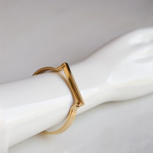 Op de afbeelding: Een gouden metalen armband met een rechthoekig balkontwerp.