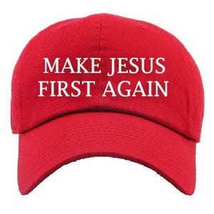May include: A red baseball cap with the text "MAKE JESUS FIRST AGAIN" in white block letters. The cap has a curved brim and a structured crown. The text is centered on the front of the cap.