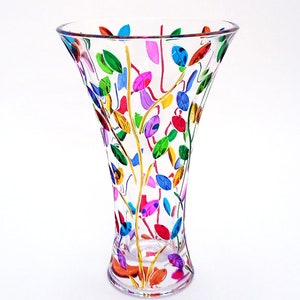 Puede incluir: Jarrón de cristal transparente con la parte superior acampanada, pintado a mano con hojas coloridas en tonos rojos, verdes, azules y morados. Las hojas están dispuestas alrededor de finos tallos dorados. El jarrón tiene una base transparente y un acabado liso y brillante.