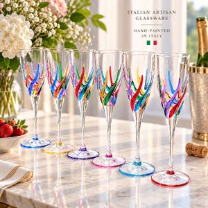 Peut inclure: Six flûtes à champagne en verre transparent ornées de motifs de vagues multicolores peints à la main en rouge, bleu, vert et jaune. Chaque pied et base est accentué par un bord en verre coloré assorti. Le texte indique : ITALIAN ARTISAN GLASSWARE.