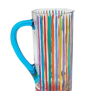 Peut inclure: Une carafe en verre transparent avec un motif rayé vertical multicolore. La carafe a une anse bleu vif et une base rouge. Le design comprend des rayures rouges, oranges, jaunes, vertes, violettes et bleues. Idéale pour servir des boissons.
