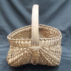 May include: A woven basket with a wooden handle. The basket is made of natural materials and has a rustic appearance.