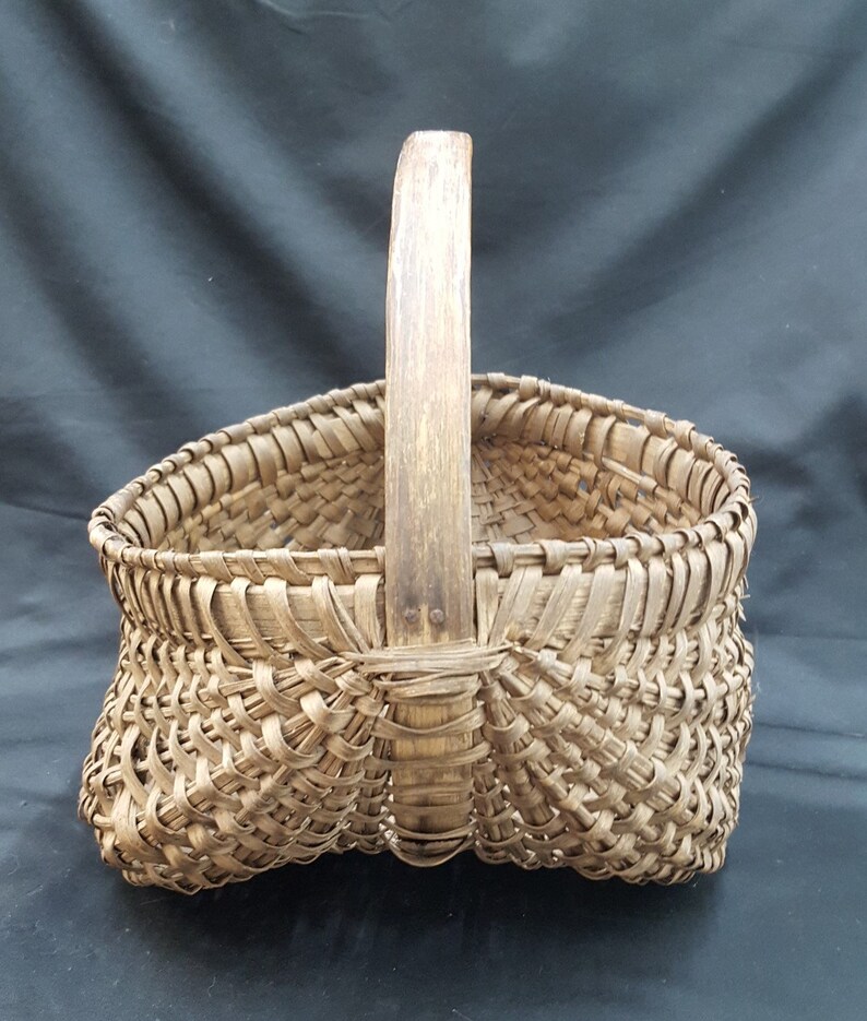 May include: A woven basket with a wooden handle. The basket is made of natural materials and has a rustic appearance.