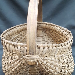 May include: A woven basket with a wooden handle. The basket is made of natural materials and has a rustic appearance.