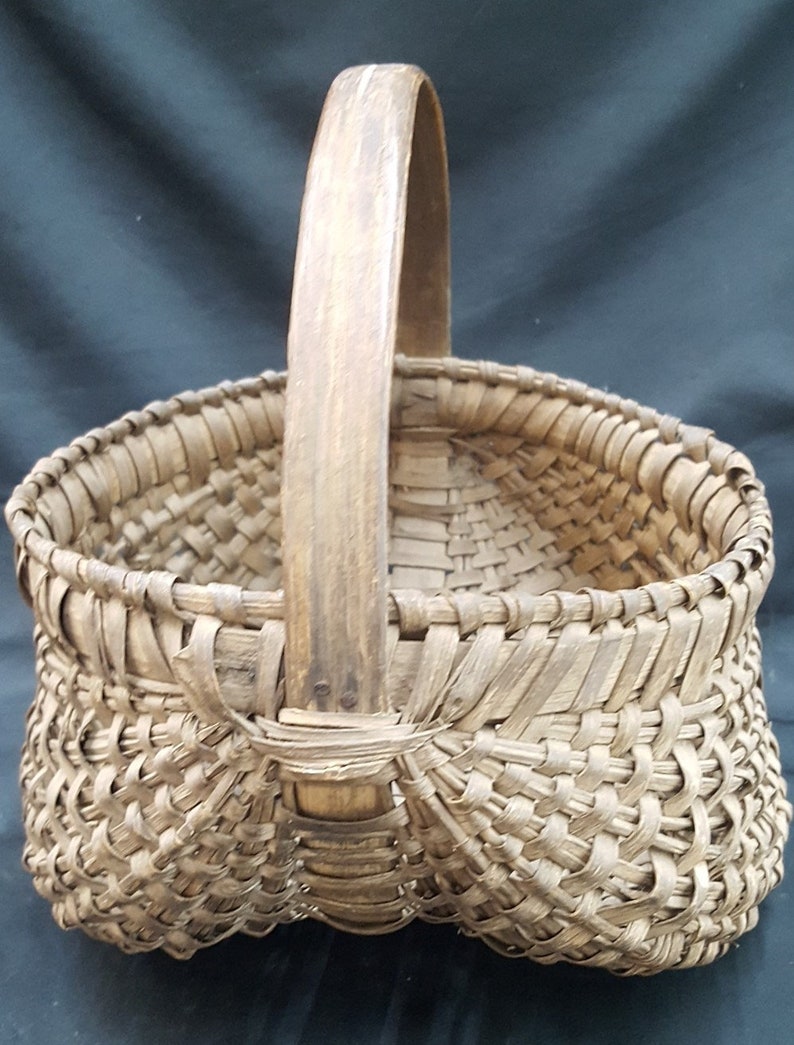 May include: A woven basket with a wooden handle. The basket is made of natural materials and has a rustic appearance.