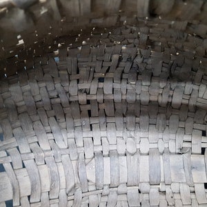 May include: Close-up of a woven basket made of natural materials. The basket is made of thin strips of wood that are woven together in a tight pattern. The basket is brown in color and has a slightly rough texture.