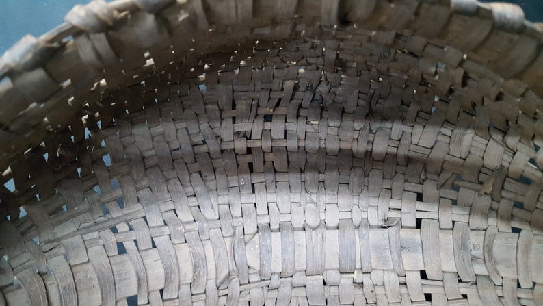 May include: Close-up of a woven basket made of natural materials. The basket is made of thin strips of wood that are woven together in a tight pattern. The basket is brown in color and has a slightly rough texture.