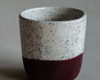 May include: A white ceramic mug with black speckles and a burgundy band around the bottom.
